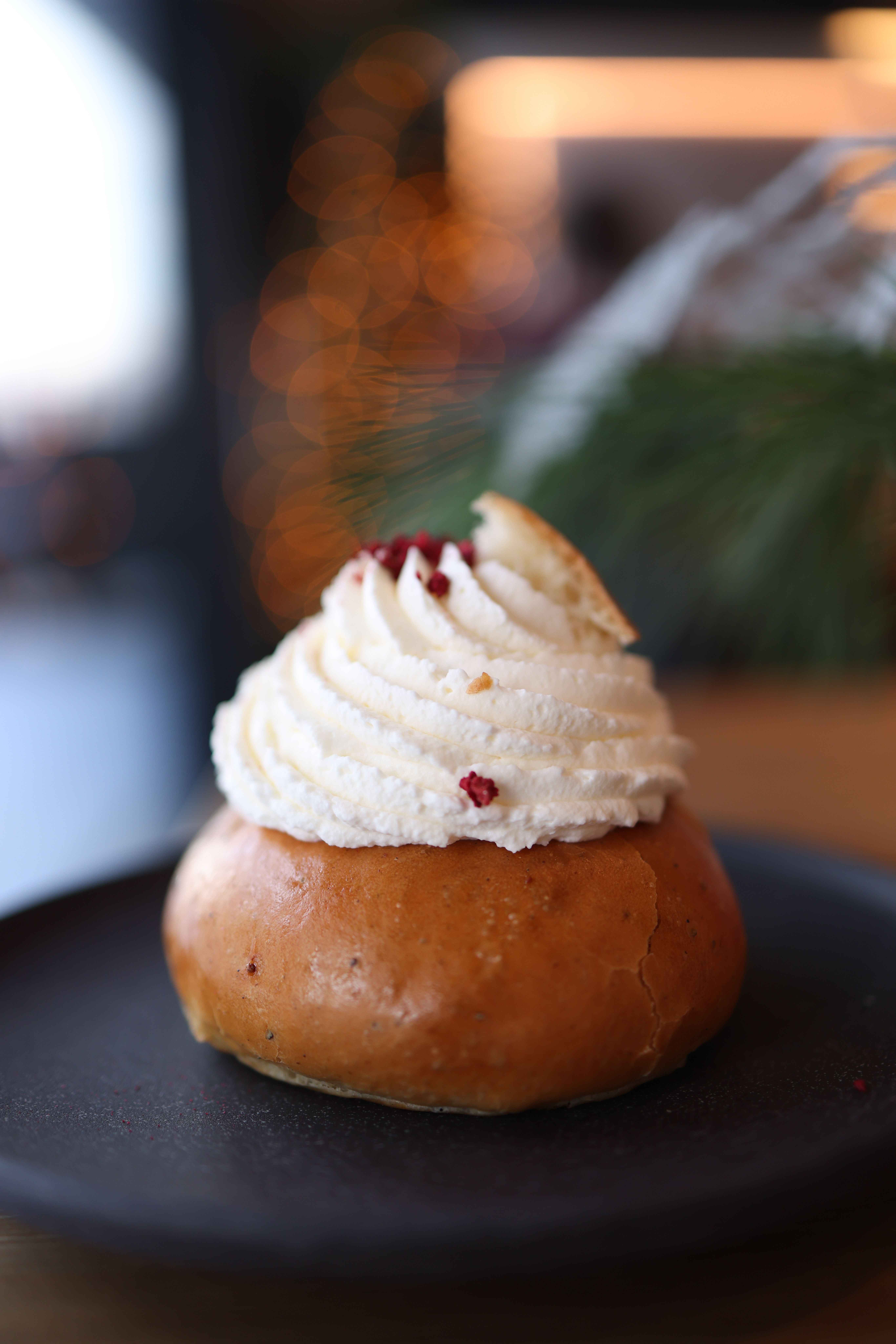 Close-up of a sweet bun topped with creamy icing on a black plate.