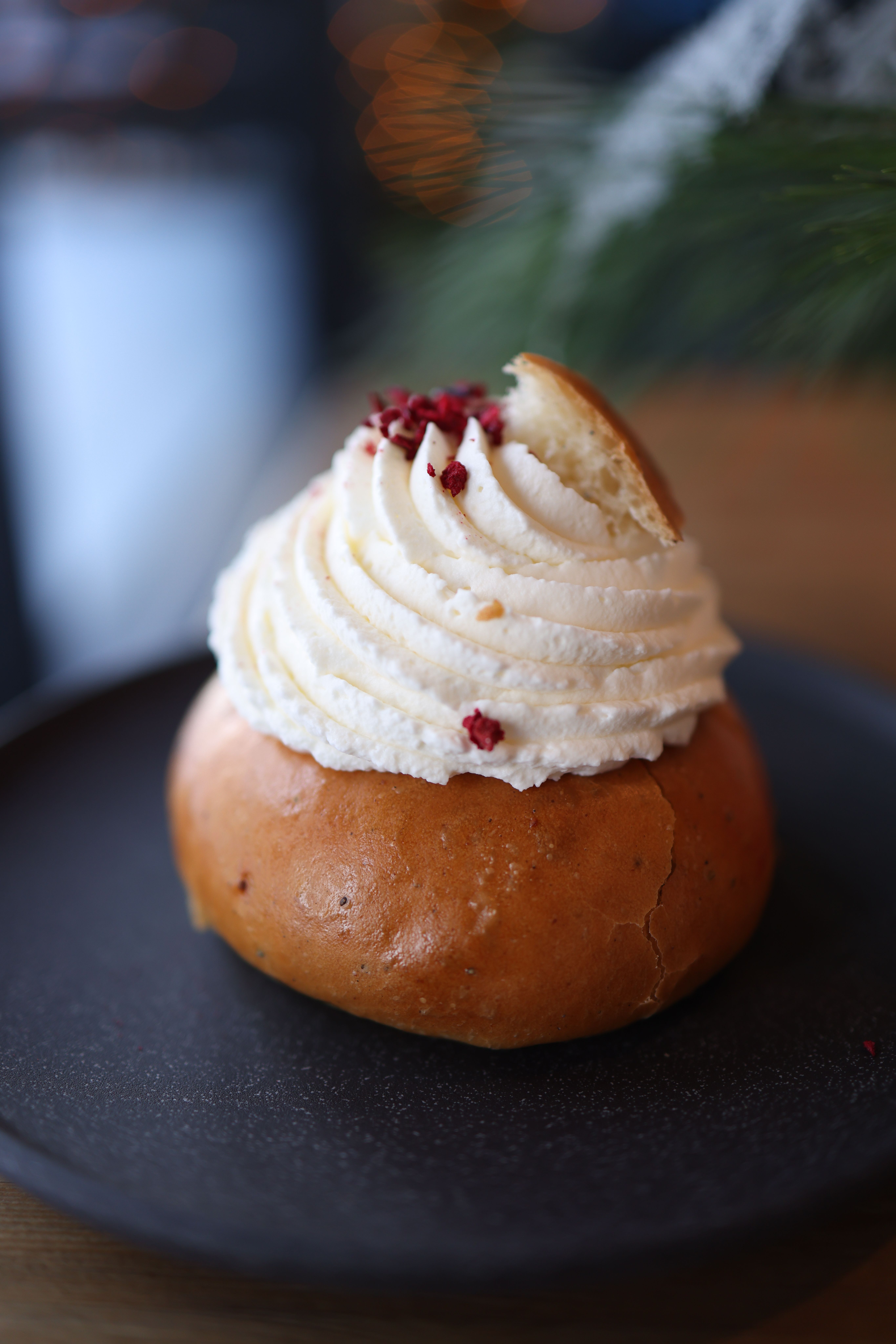 Close-up of a fresh pastry with whipped cream topping on a dark plate.