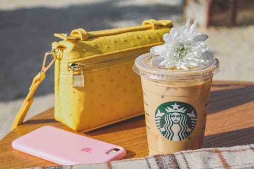 Close-up of a Starbucks Coffee, a Purse and Smartphone Lying on the Table in Sunlight 