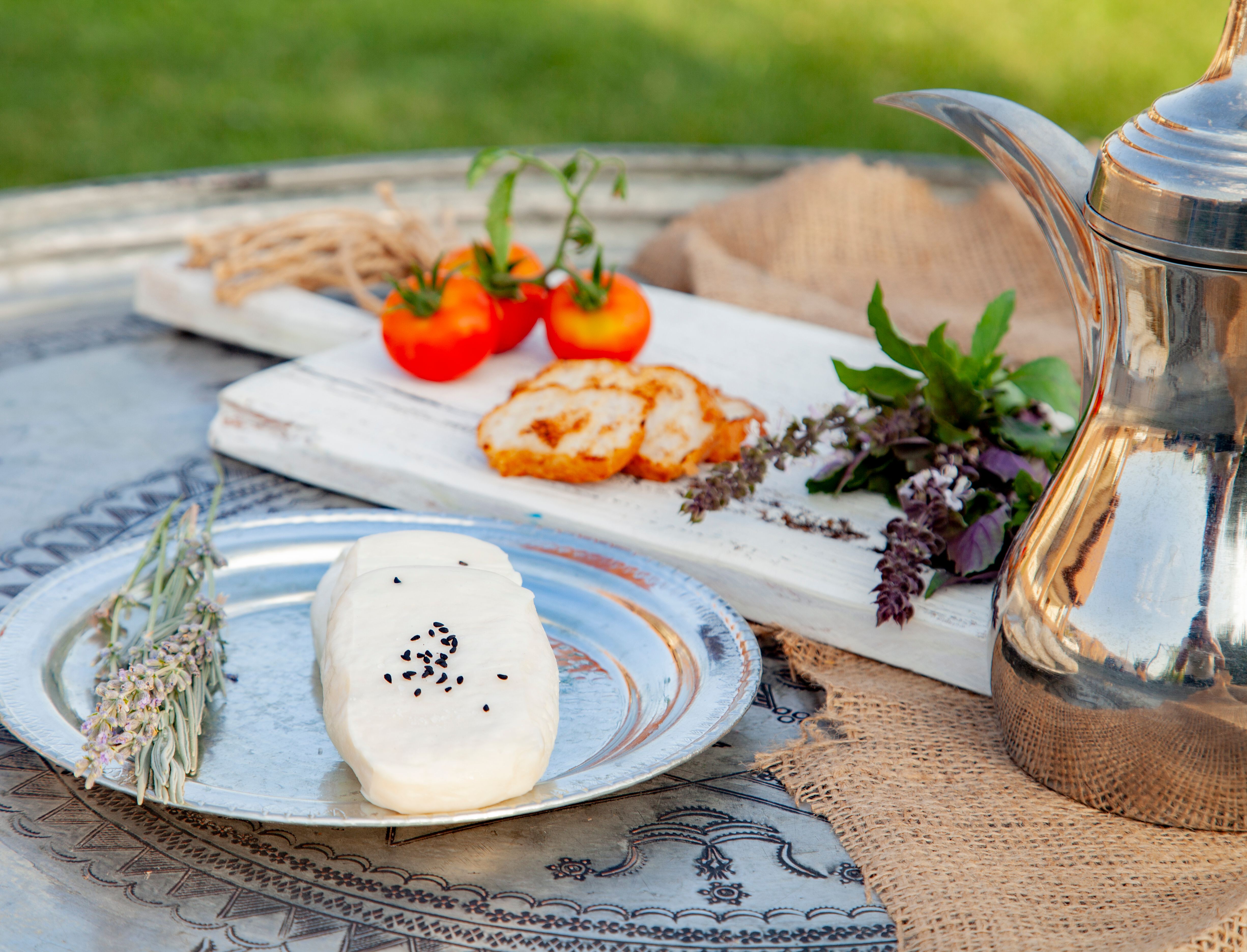 An inviting breakfast scene outdoors featuring cottage cheese with black sesame, fresh tomatoes, and herbs on a rustic table.