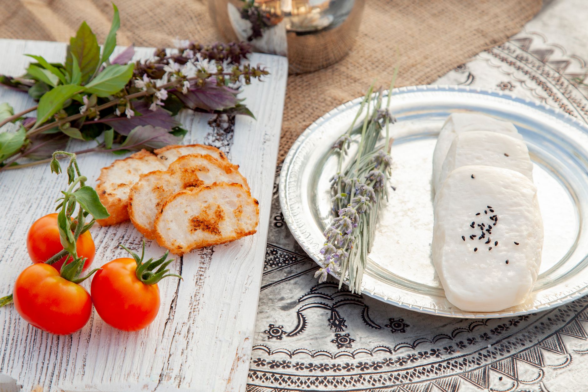 Sliced bread, fresh tomatoes, and cheese with black sesame seeds on a rustic setup.