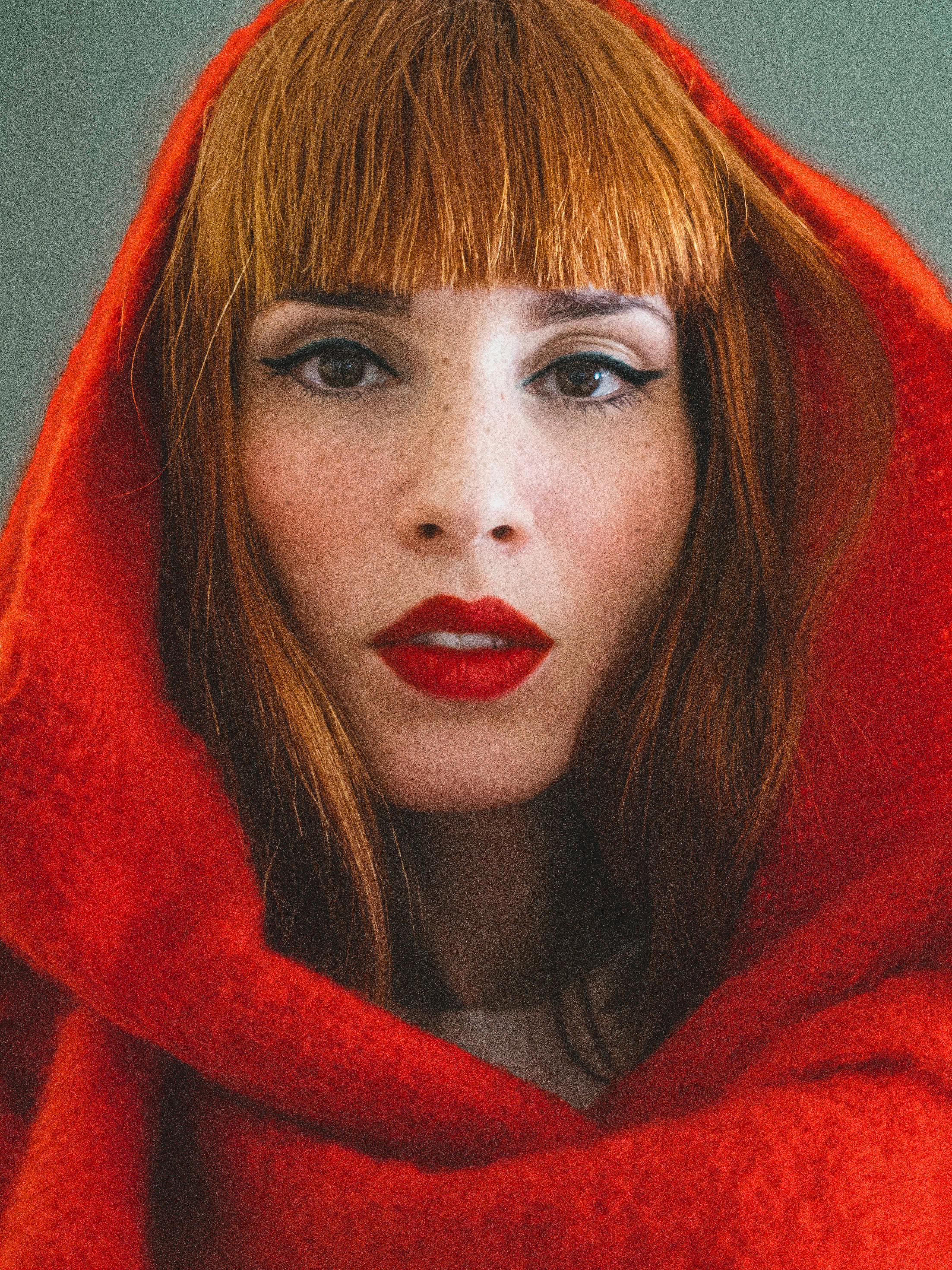 Portrait of a stunning redhead woman in a vibrant red hood, showcasing classic beauty and style.