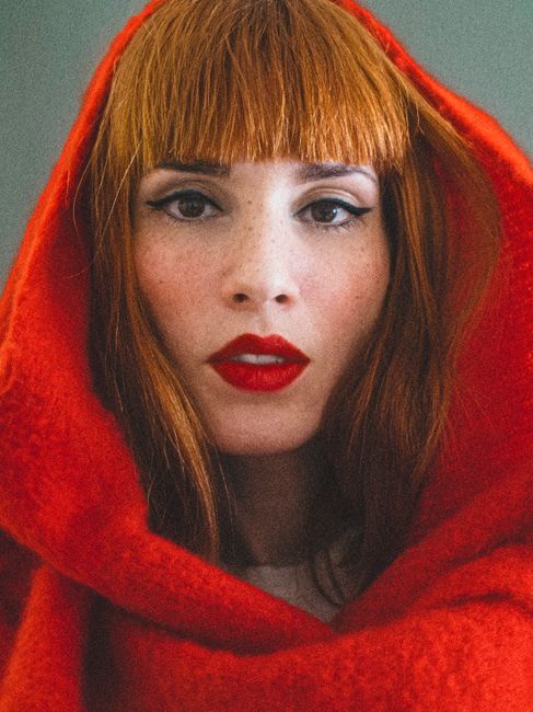 Portrait of a stunning redhead woman in a vibrant red hood, showcasing classic beauty and style.