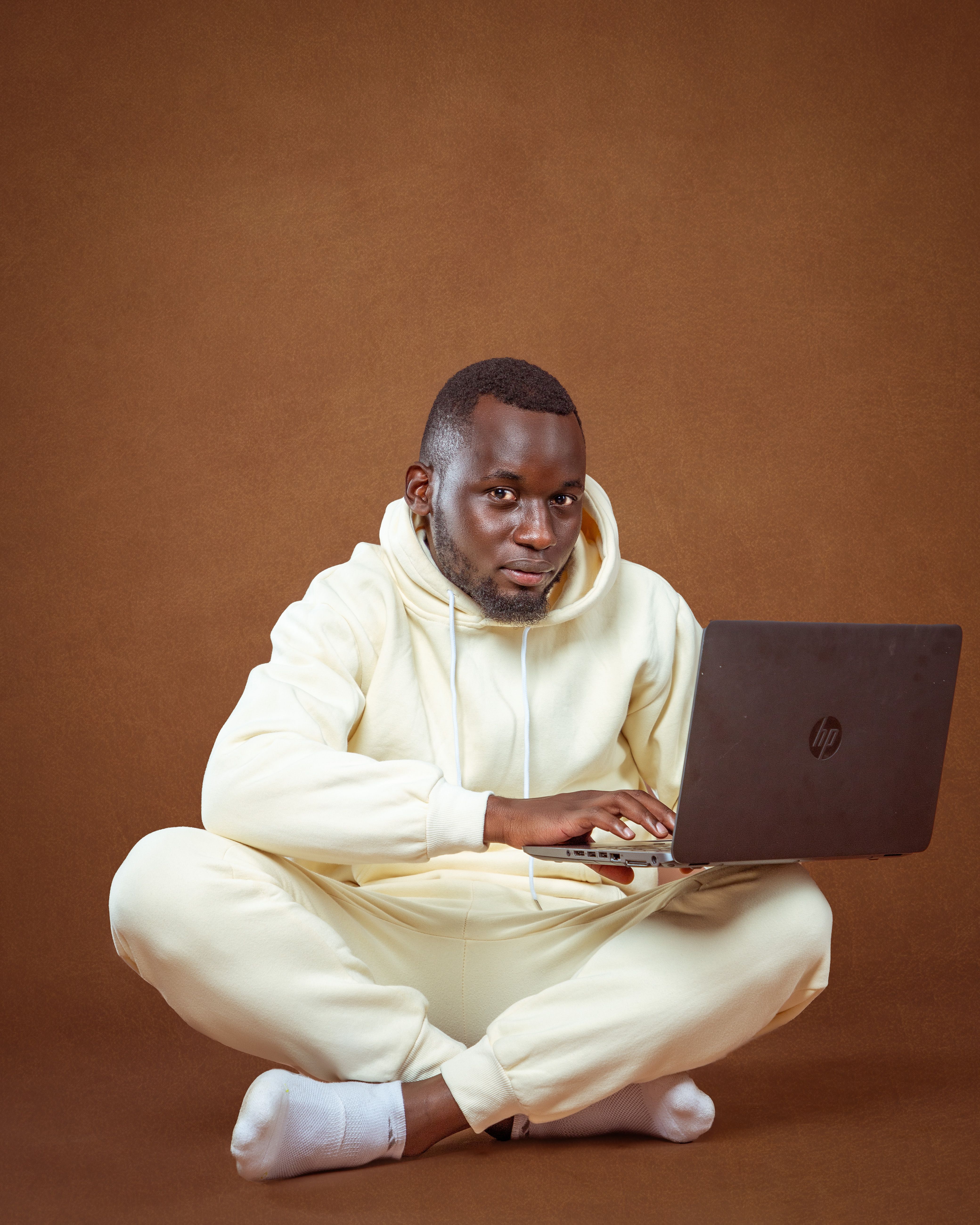 Fashionable man in a light tracksuit using a laptop against a brown background. Studio portrait.
