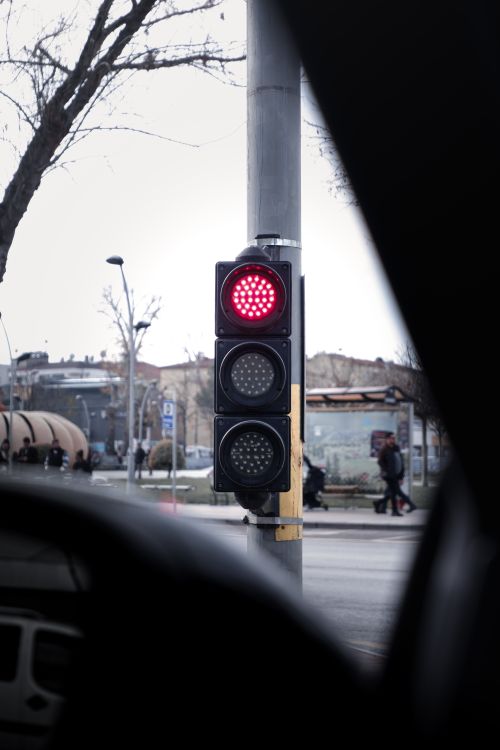 Free Capture of a red traffic light in an urban setting with pedestrians and overcast skies. Stock Photo