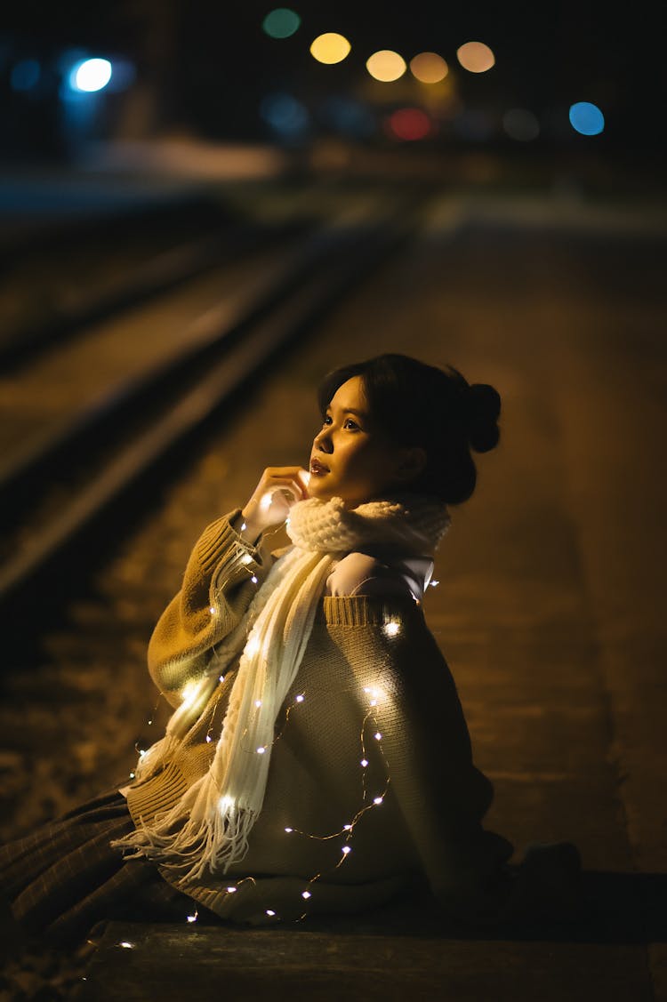 Woman With Lights And In Scarf Sitting On Railway Track At Night