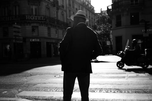 Black and white silhouette of a man with a hat in a Parisian street.