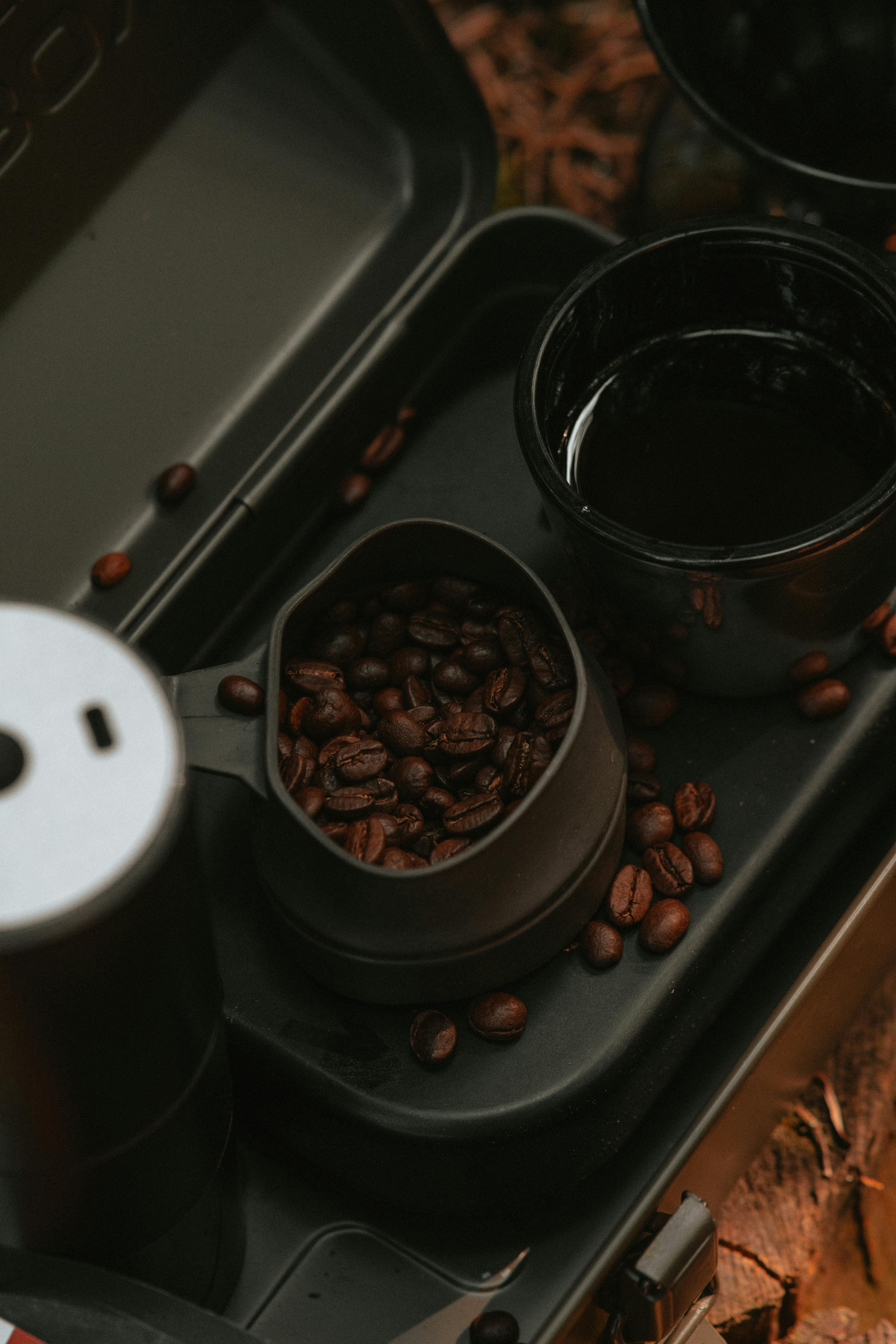 A moody close-up of coffee beans and cups in a portable camping coffee maker.
