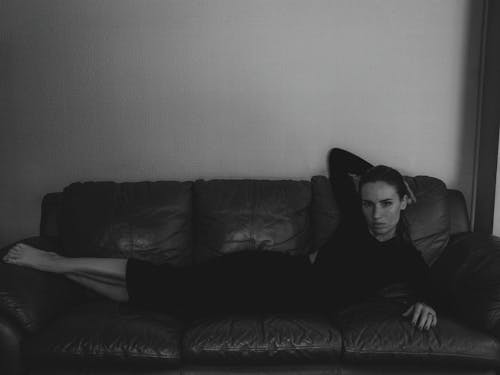 Woman in Black Clothing Lying on Leather Couch