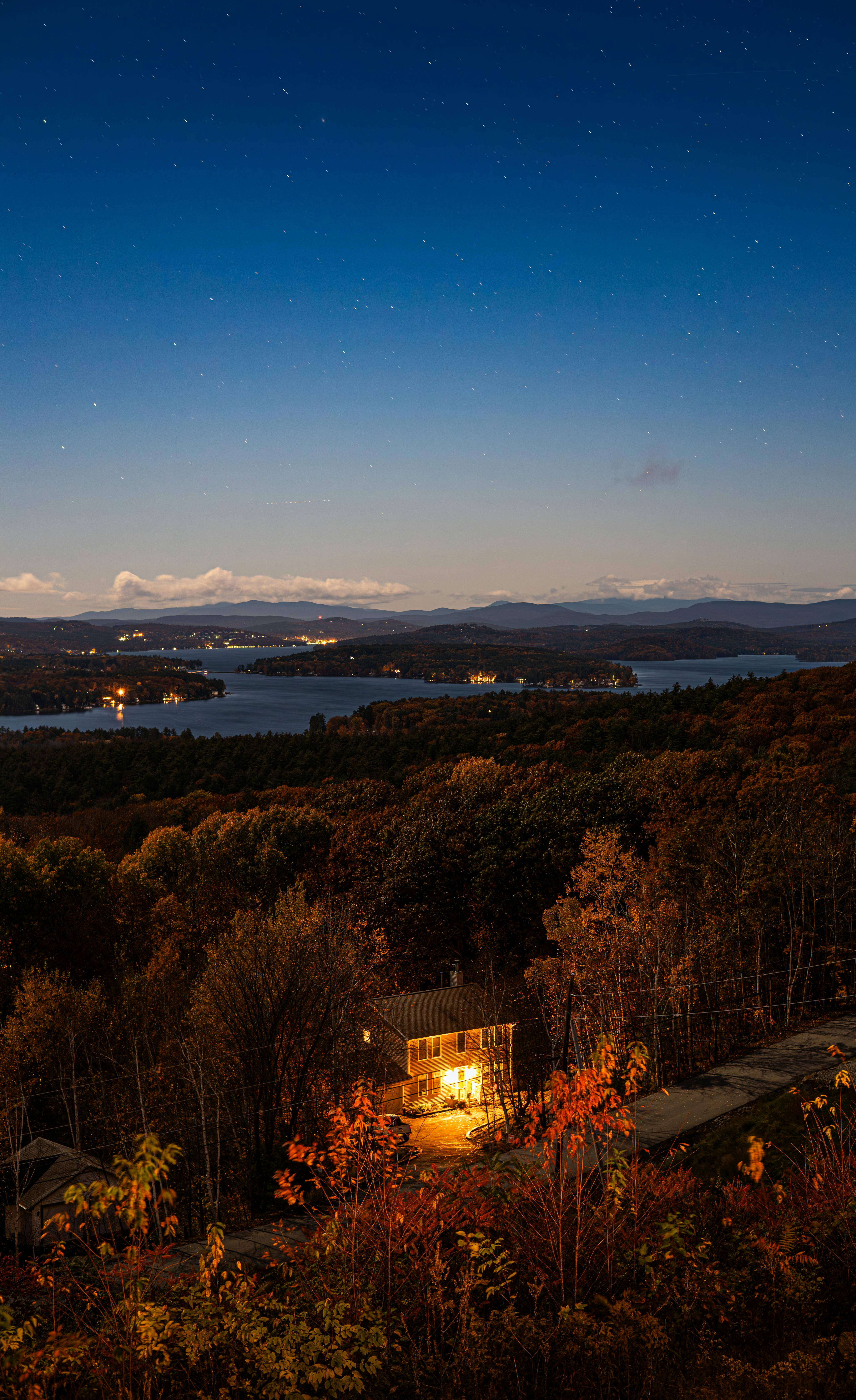 A picturesque twilight aerial view of a house, forest, and lake under a starry sky.
