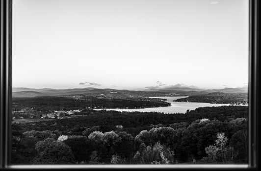 Monochrome view of a scenic river and forested hills through a window, creating a peaceful landscape.