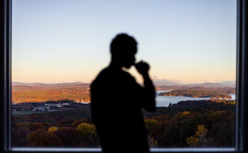 Free Person Drinking from a Mug Overlooking a Landscape Through a Window Stock Photo