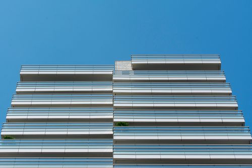 Free Low angle view of a modern building with glass balconies and a clear blue sky. Stock Photo