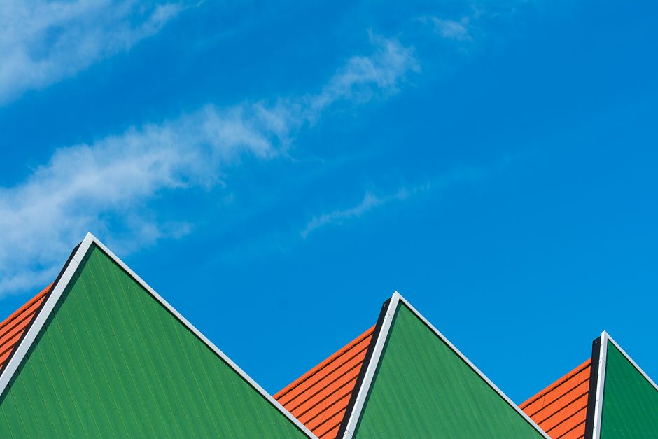 Vibrant green triangular rooftops aligned under a clear blue sky, capturing a modern architectural style.