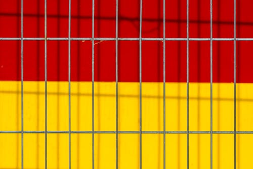 Close-up of a Metal Fence on the Background of a Red and Yellow Wall 