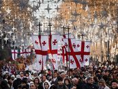 Crowds march in Tbilisi under flags and stars during a festive parade.