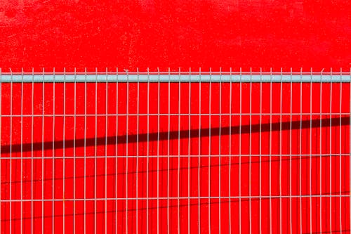Close-up of a Metal Fence on the Background of a Bright Red Wall 