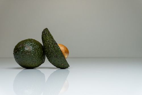 Free A minimalist photo of an avocado halved on a reflective surface, showcasing its texture and seed. Stock Photo