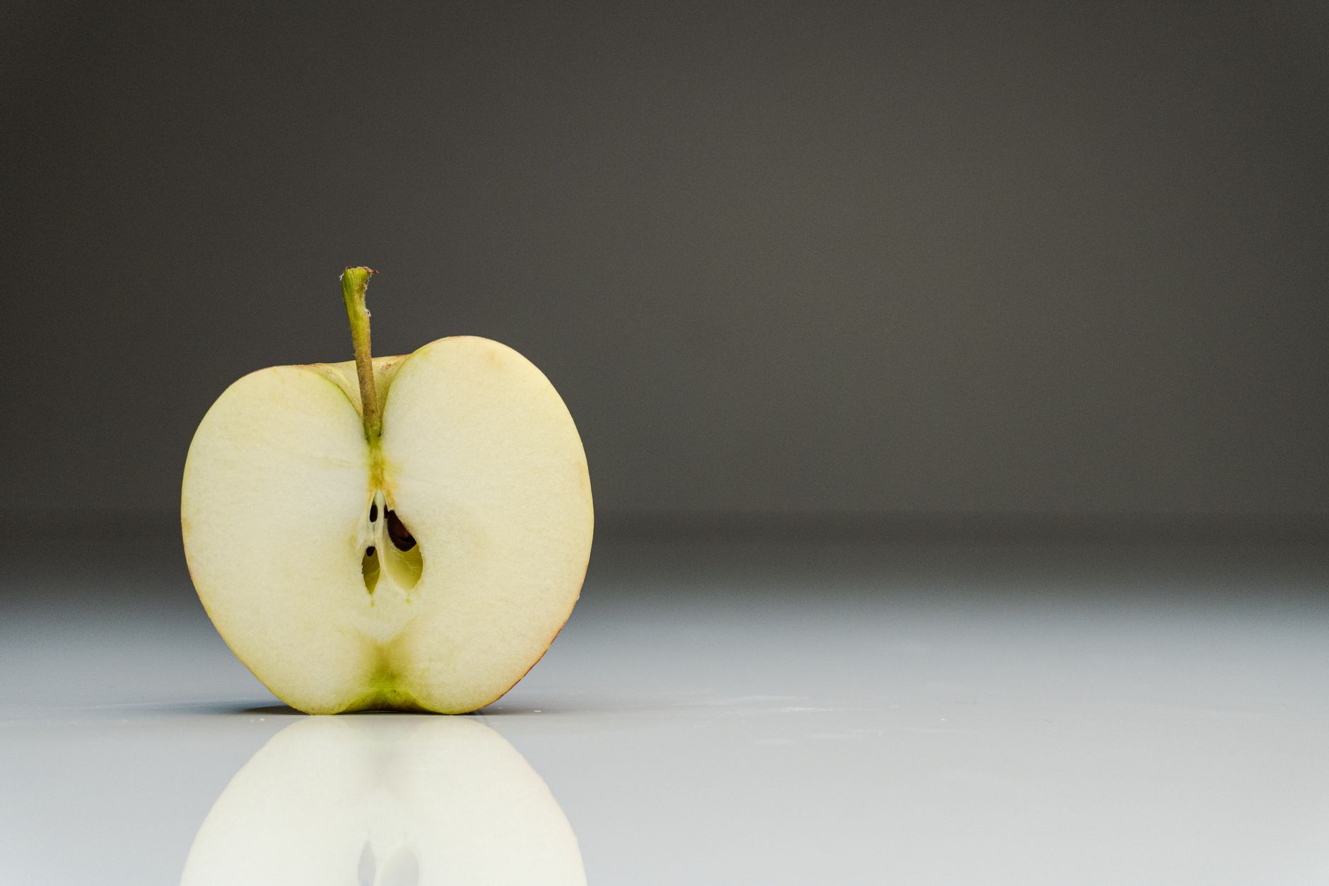 A clean minimalist close-up of a halved apple on a reflective surface, showcasing its organic texture.