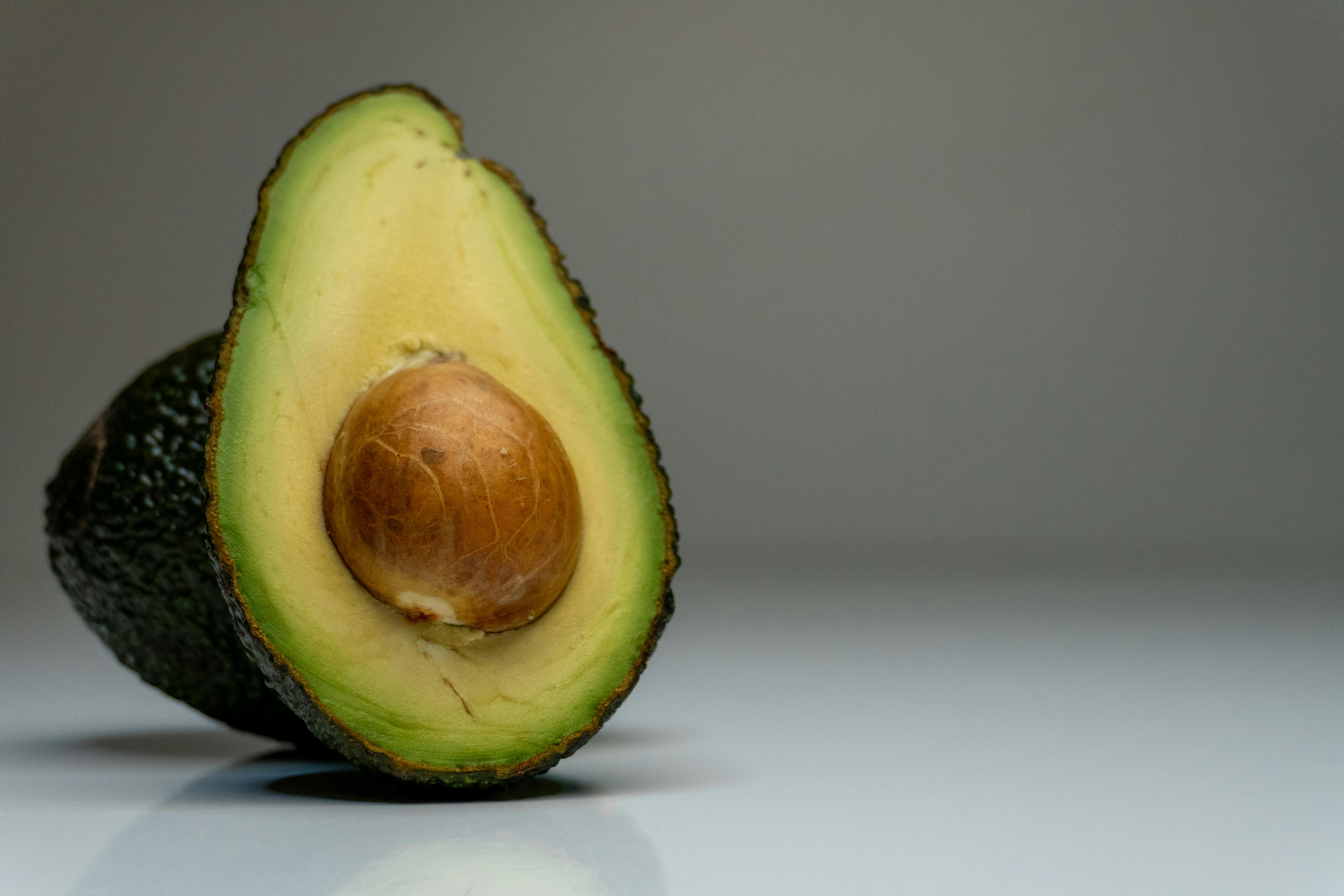 Half avocado on gray background, showcasing fresh green and brown hues for food photography.