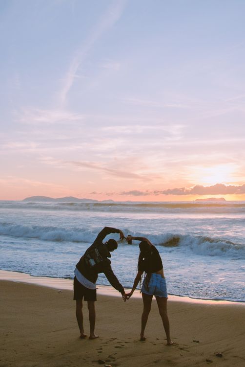 Couple Making a Heart Shape while Looking at the Sunrise over the Ocean ...