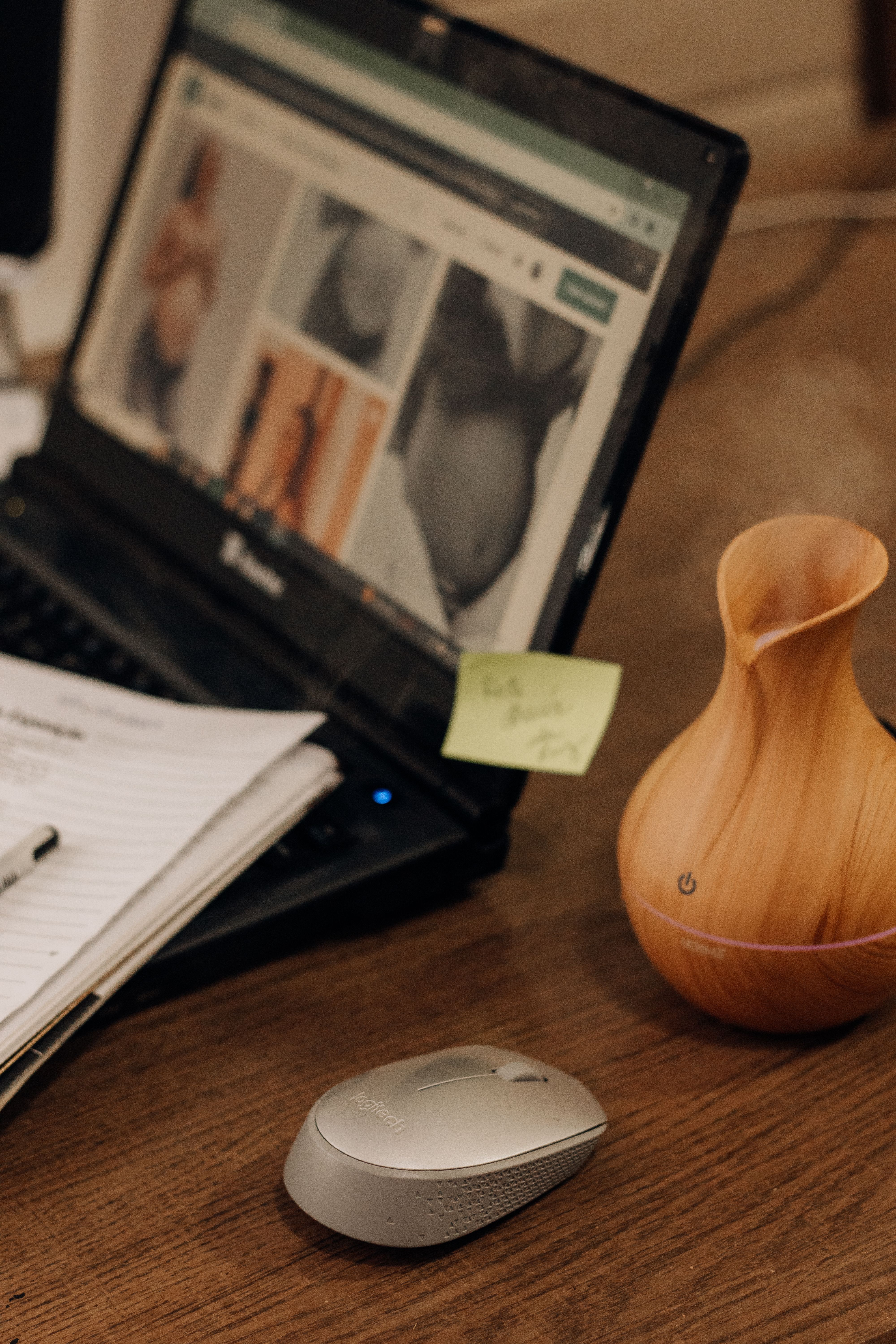 A cozy desktop setup featuring a laptop, mouse, notebook, and a vase on a wooden desk.