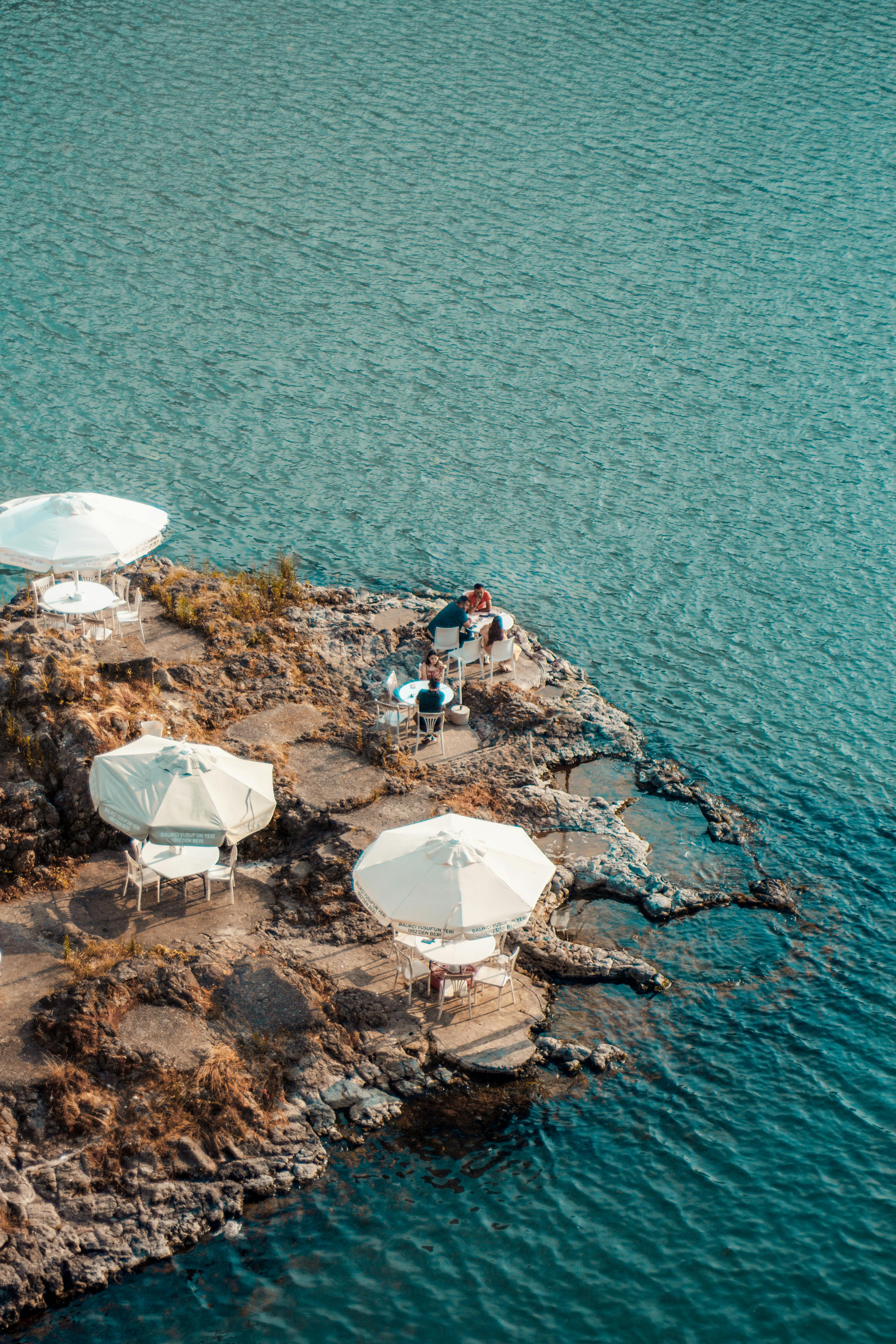 An aerial view of a rocky peninsula with white umbrellas and chairs set against a calm sea.