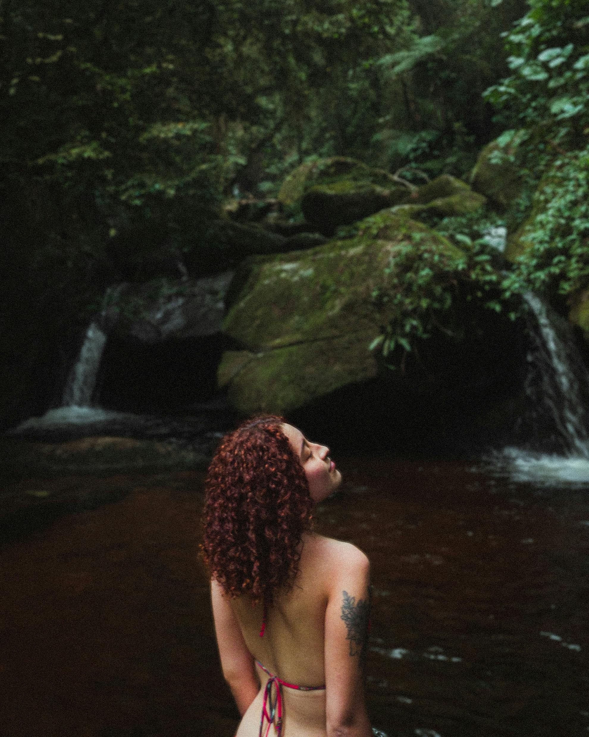 Woman enjoying a peaceful moment by a waterfall in a lush forest setting, capturing a tranquil escape to nature.