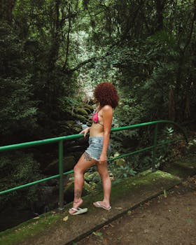 A woman stands thoughtfully by a railing in a lush forest, embracing the tranquility of nature.