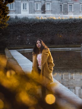 日落时分，宁静花园的反射池边，一位身着舒适外套的妇女构成了画面