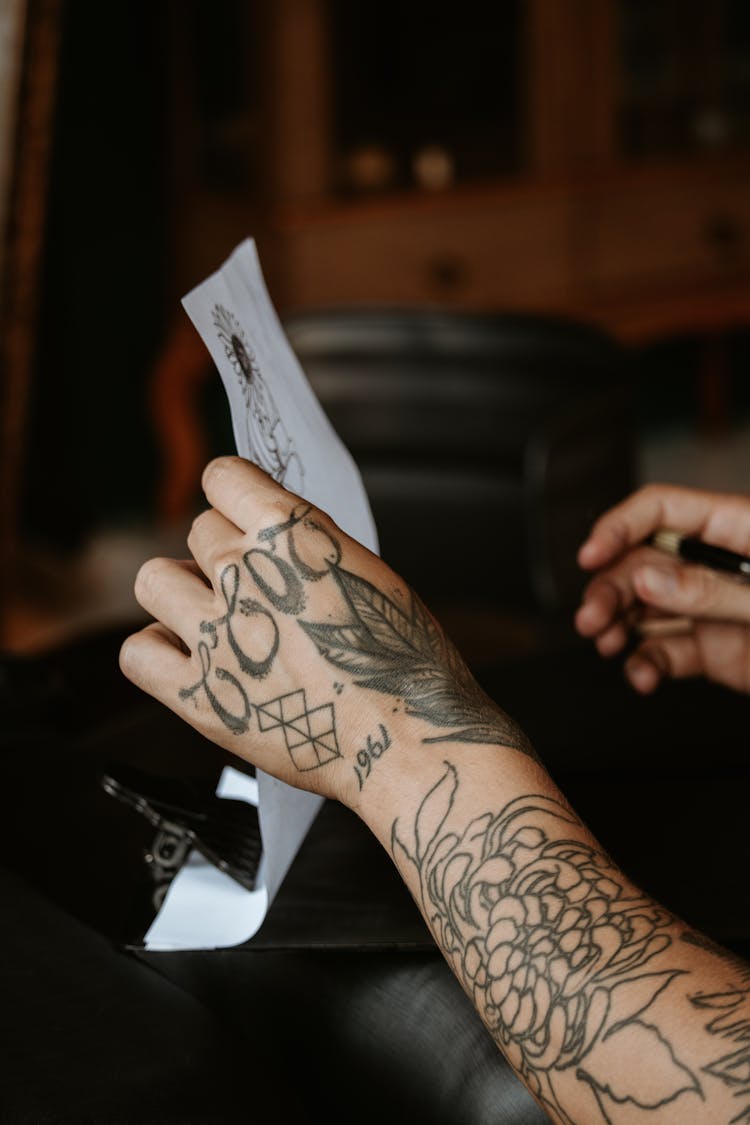 Hand With Tattoos Holding Paper Sketch