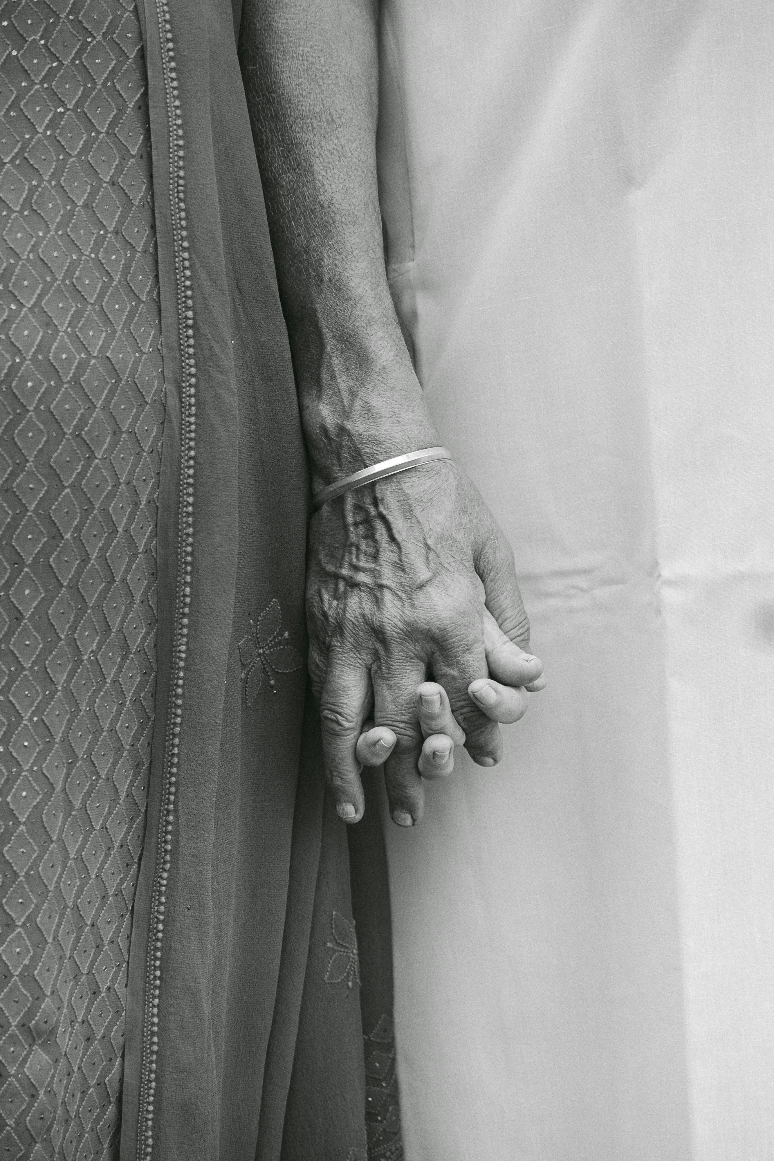 A close-up black and white photo of a couple holding hands with traditional attire in Surat, India.