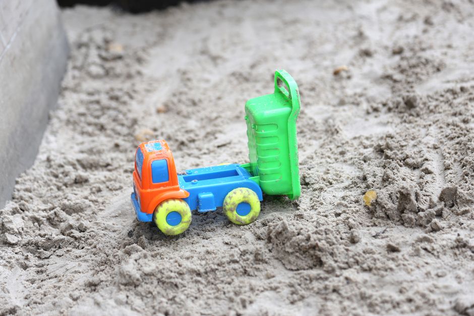 A bright toy truck lies on a sandy playground surface, showcasing vibrant colors and childlike fun.