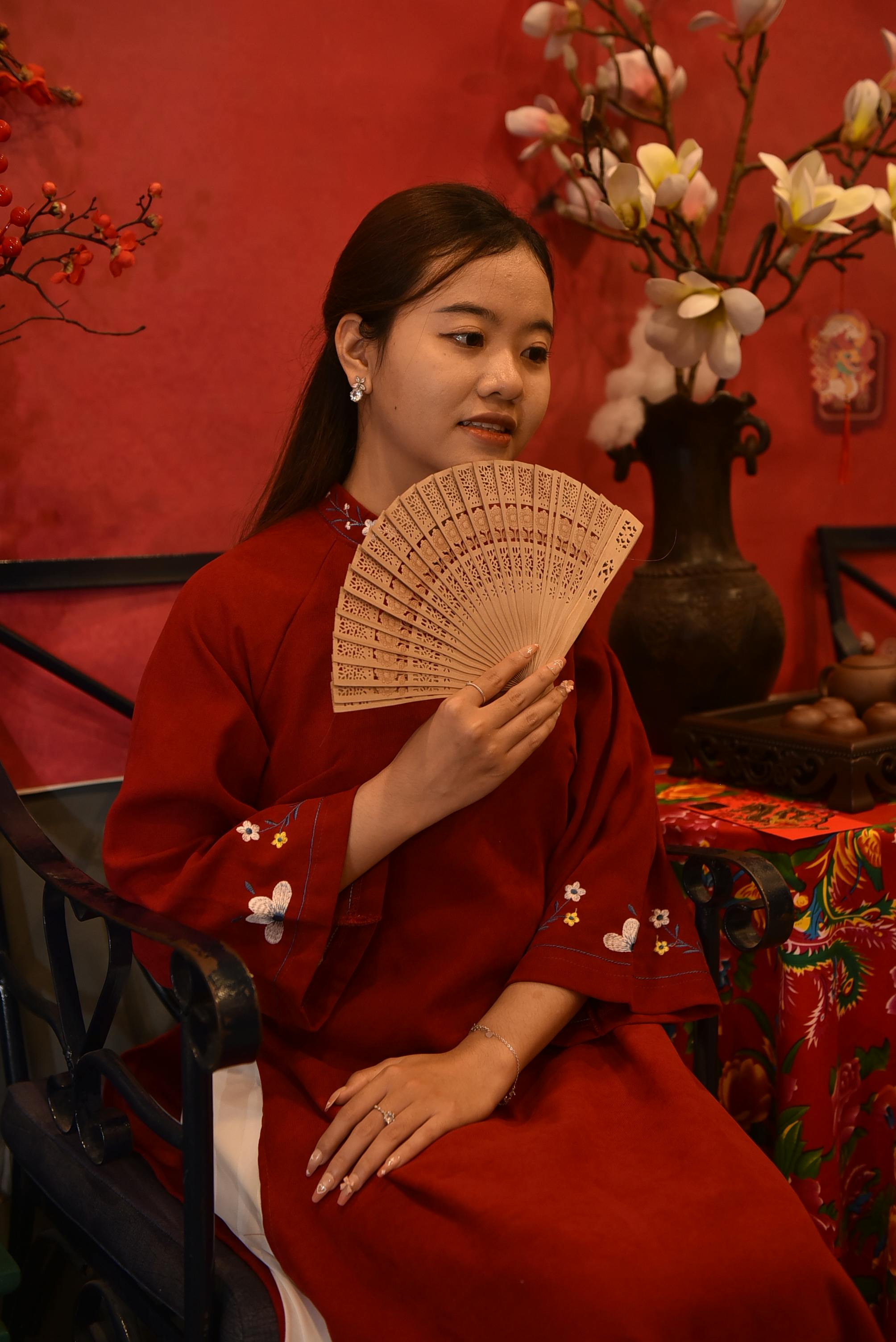 [ColoSach]-a-woman-elegantly-dressed-in-traditional-red-attire-holding-a-fan,-sitting-gracefully-with-a-serene-expression.