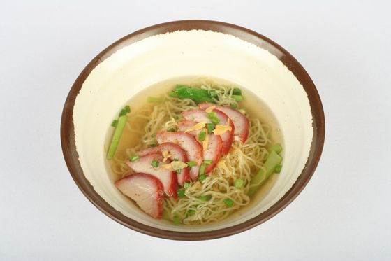 Bowl of thin egg noodles in clear broth topped with red-edged char siu slices and scallions