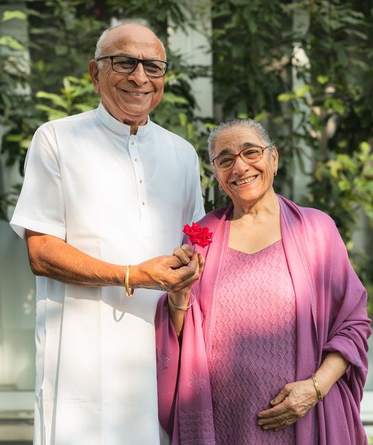 Charming portrait of a senior couple wearing eyeglasses, holding a flower and smiling together.