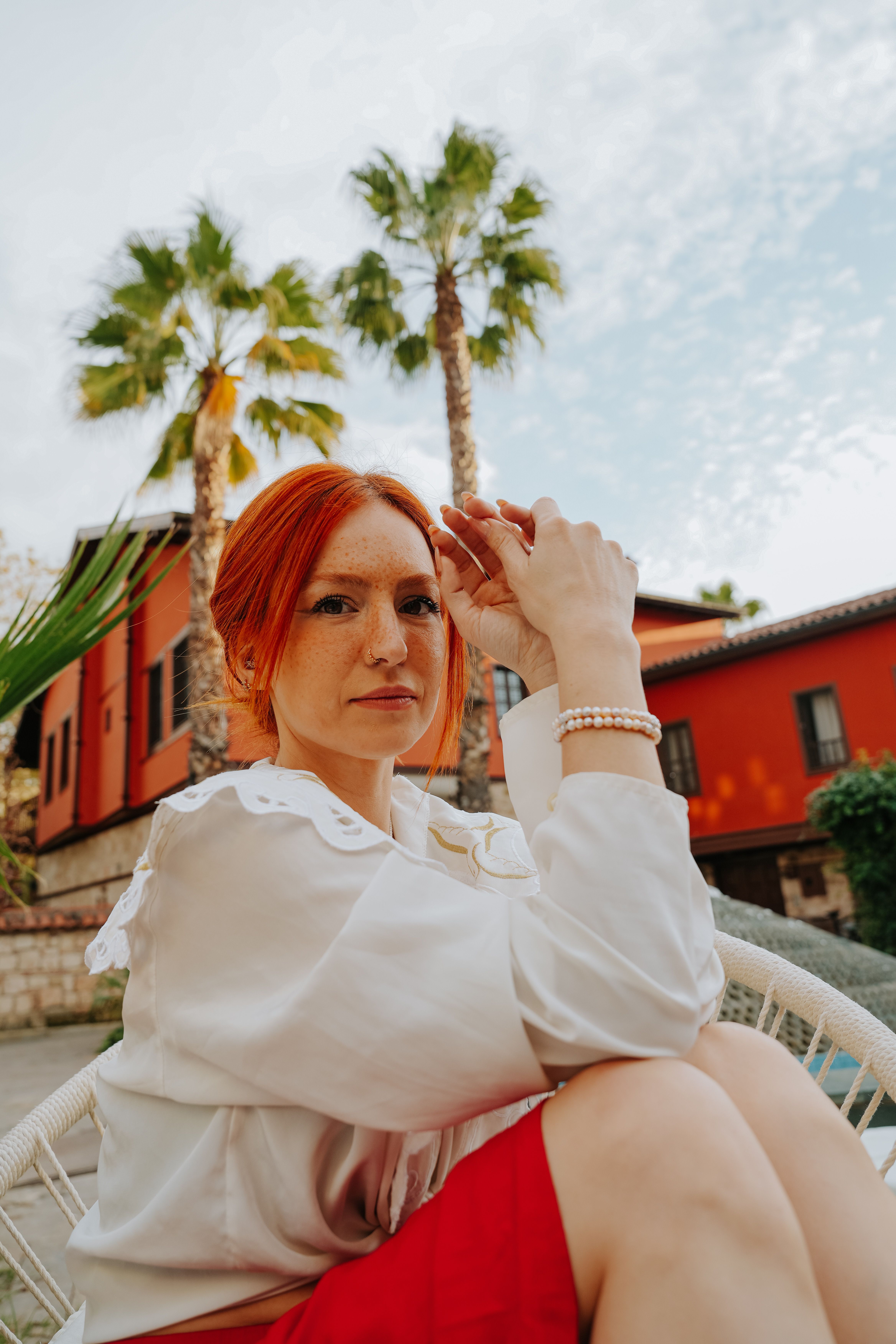 Redheaded woman in outdoor setting wearing white shirt, showcasing modern fashion style.