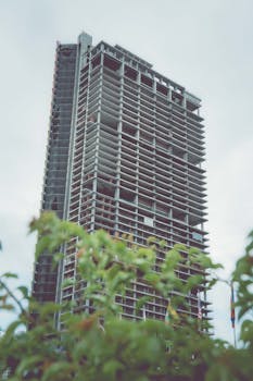 A skyscraper under construction in Ho Chi Minh City, Vietnam with lush greenery in the foreground.