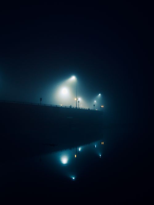 Free A foggy night scene of a bridge in Sagar, India with streetlights reflecting on the water. Stock Photo