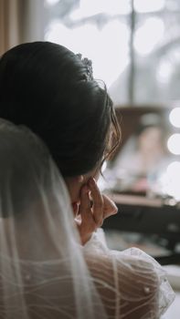 Bride with veil gazing out window, captured in serene wedding moment.