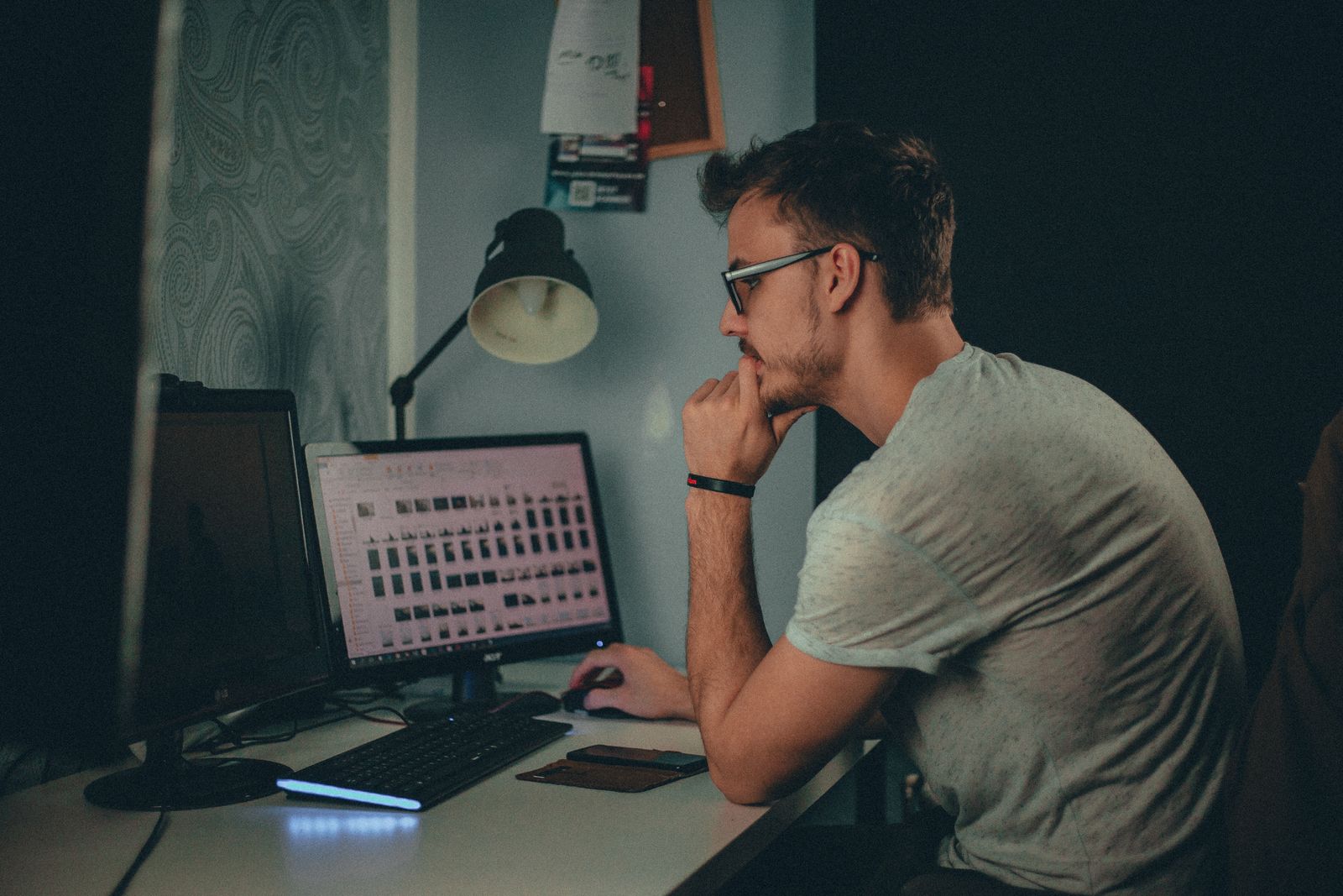 A person reviewing files at a desktop in a dimly lit workspace