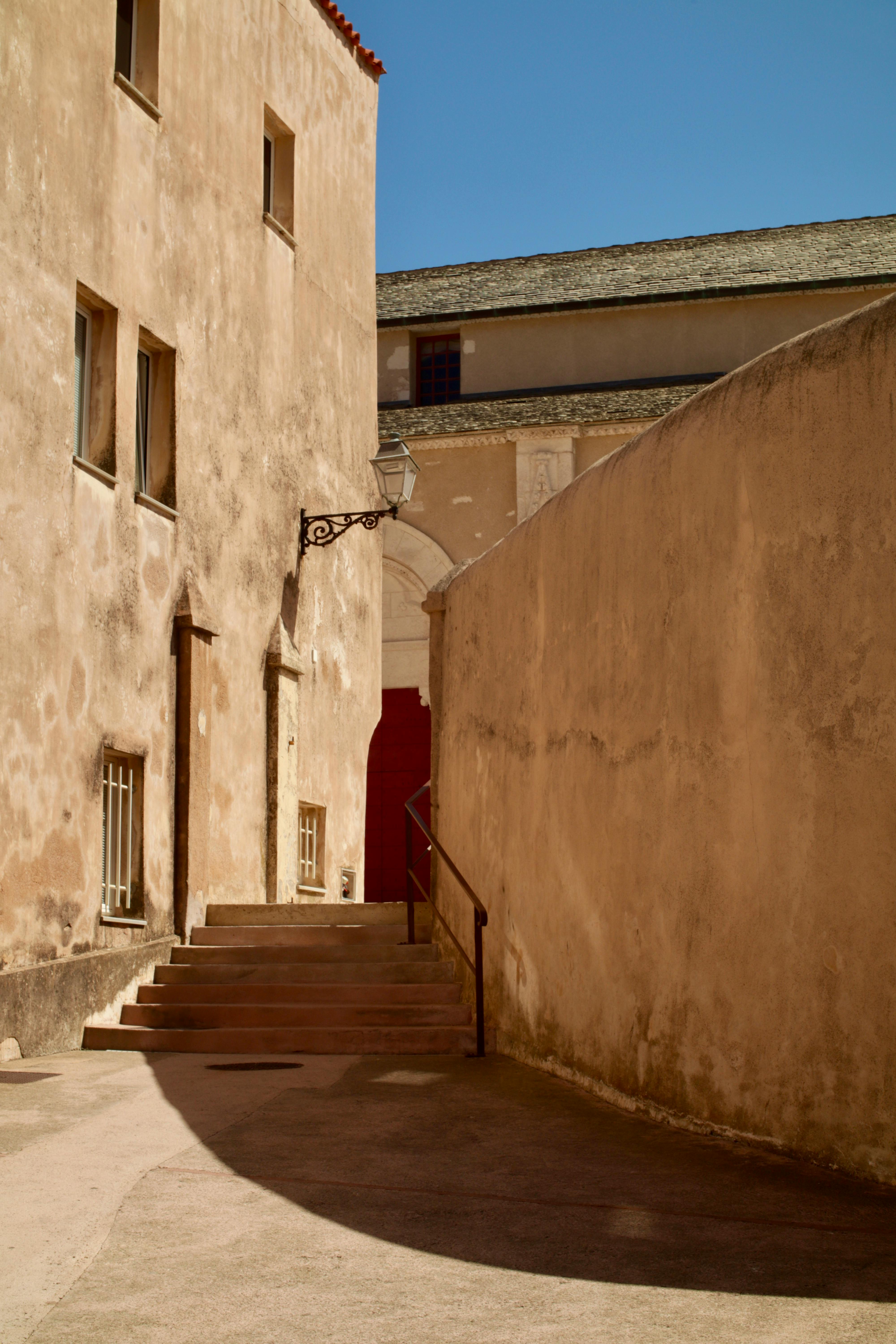 Sunlit view of Bonifacio's historic alleyway, showcasing rustic architecture and shadows.