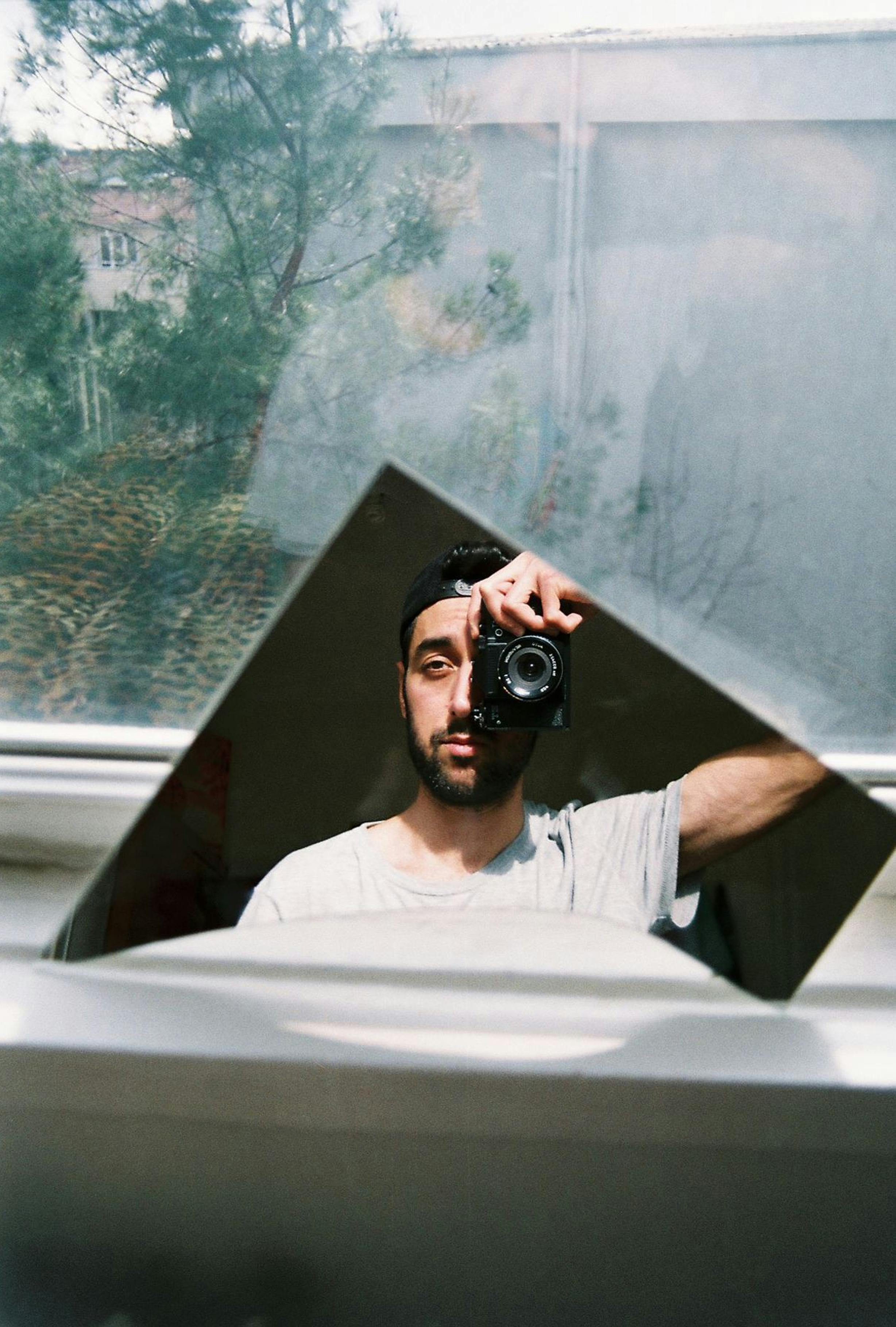 A man photographs himself using a mirror, capturing his image with a camera.