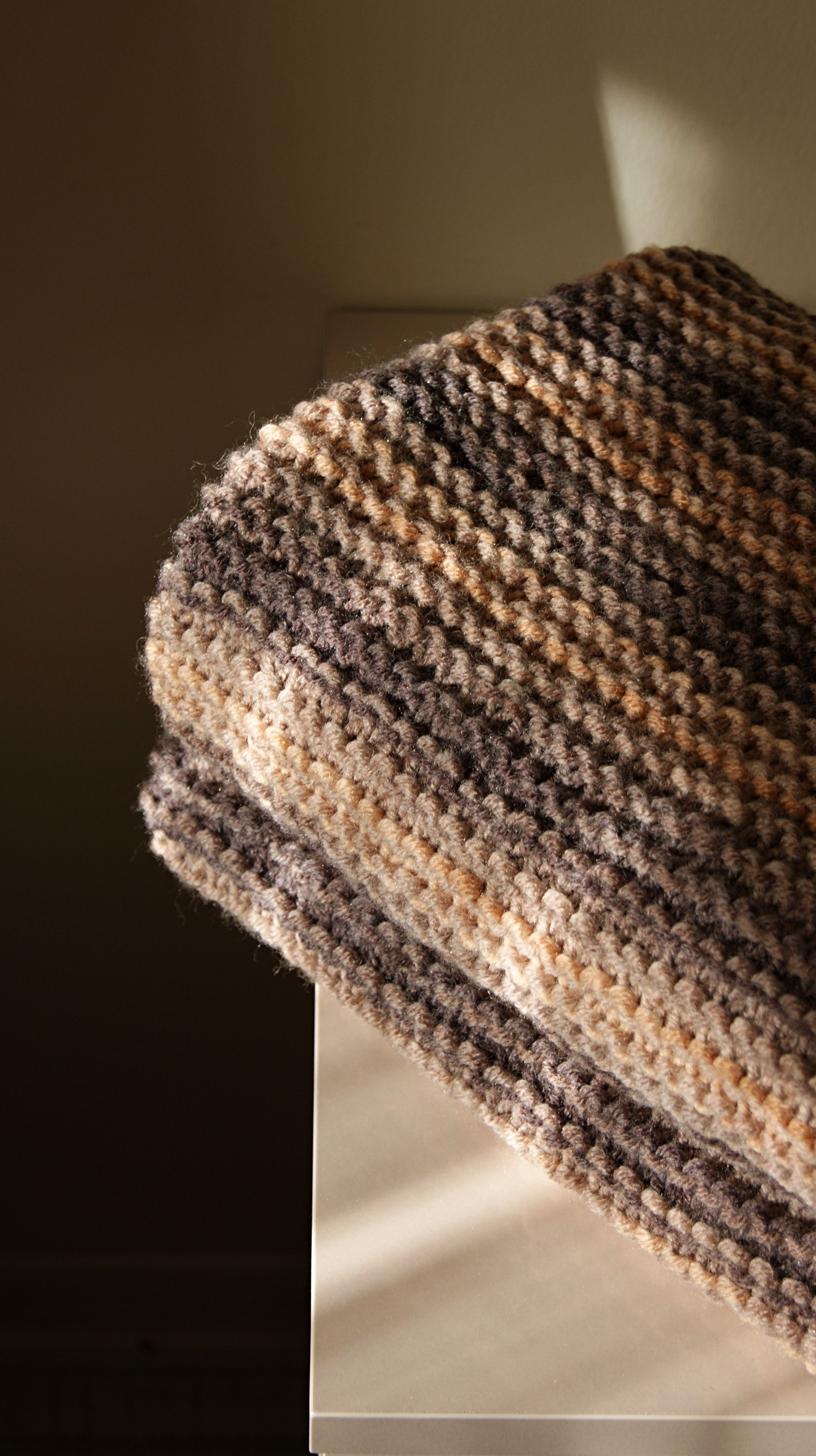 Close-up of a folded knitted shawl with crochet detailing in warm tones, captured in soft light.