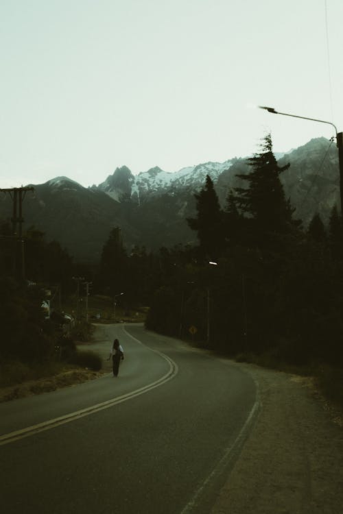 Person Walking Alone on Road in Forest Near Mountain