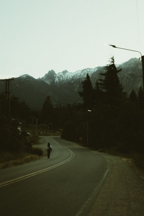 Free Solitary traveler walking along a winding road in Bariloche with mountains in the background. Stock Photo