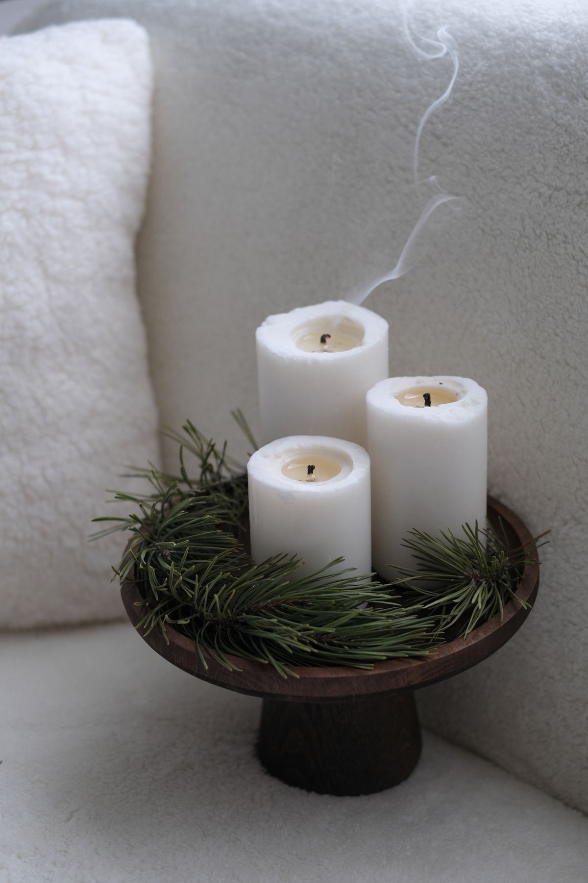 A candle display with cut pine branches on a wooden tray, a simple way to scent a room without a plug-in freshener
