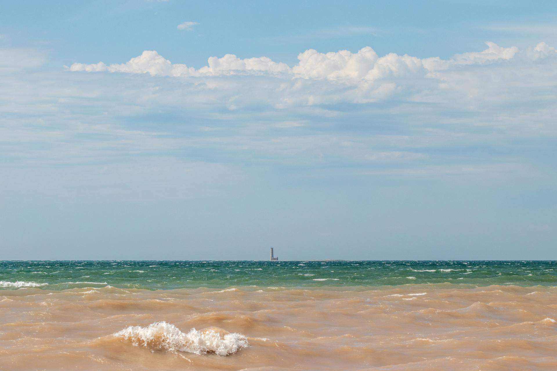 A tranquil view of Lake Erie with the distant Mohawk Island Lighthouse under billowing clouds.