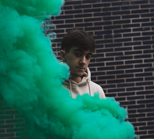 Young Man in Hoodie Standing by Green Smoke