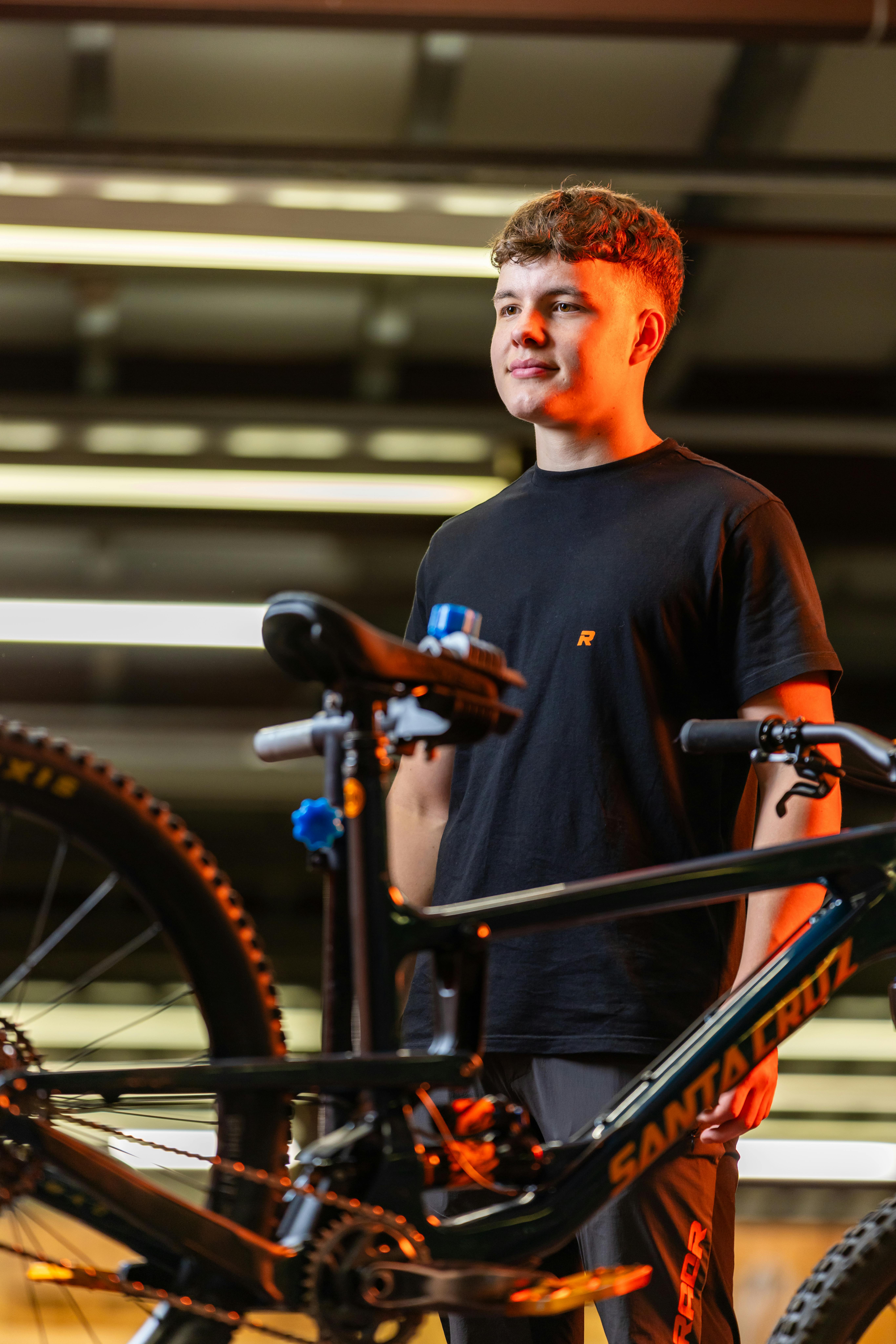 Young man standing confidently in a workshop alongside a high-end mountain bike.